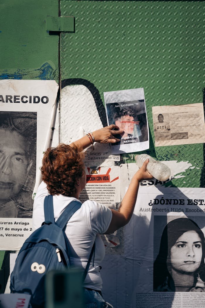 A woman places posters on a green urban wall in Mexico City, highlighting social awareness.